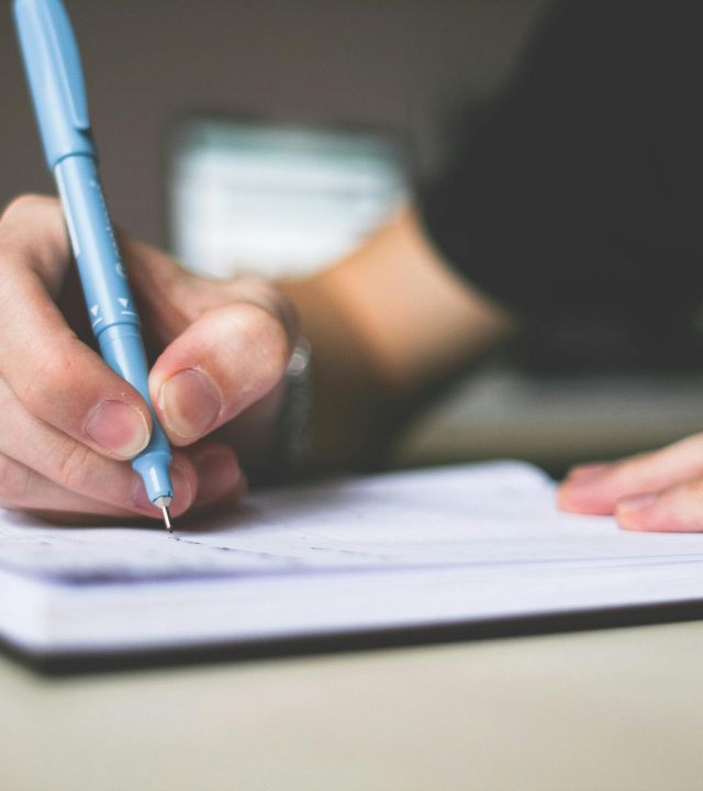 Close-up of hand writing in notebook using a blue pen, focus on creativity.